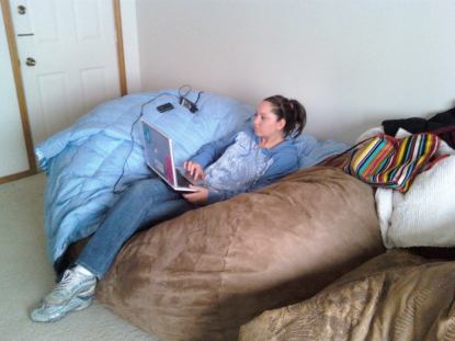 A picture of a woman on her laptop sitting comfortably in the center of a brown, giant Fombag