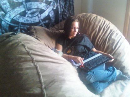 A picture of a girl with a keyboard resting comfortably against a pillow in the middle of a brown, giant Fombag