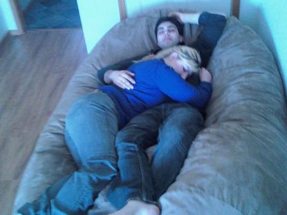 A picture of a couple, man and woman, cuddling together on a brown, giant Fombag