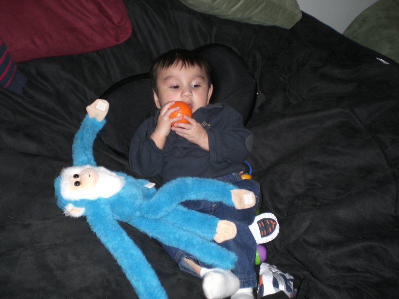 A picture of a young child, and his stuffed monkey, sitting comfortably on a dark brown, giant Fombag
