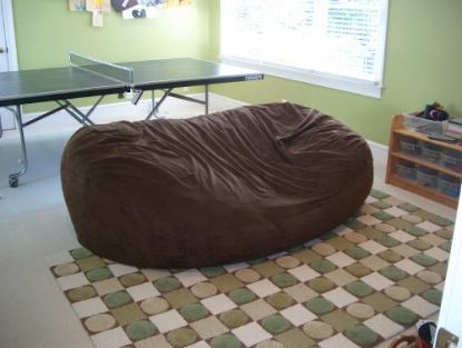 A picture of a giant, brown Fombag in the center of a room with table tennis set up behind it