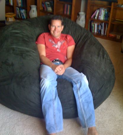 A picture of a middle aged man sitting in the center of a giant, grey Fombag