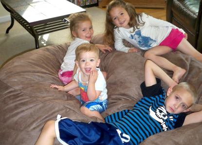 Four young children sitting all across a giant Fombag smiling