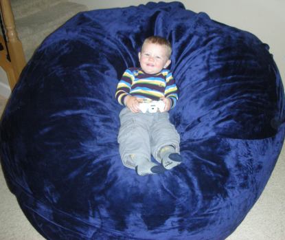 A young child, around the age of 2, sitting in the center of a giant, blue Fombag