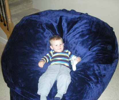 A young child slouching in a giant, blue Fombag while holding an Xbox controller