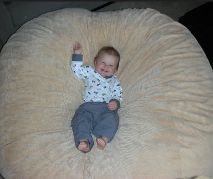 A small baby smiling as he lies in the center of a giant, tan Fombag