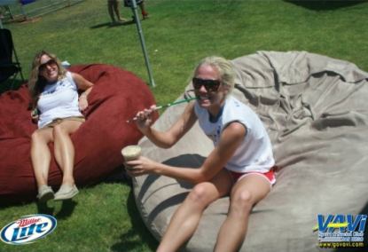 Two woman sitting on two separate 6' Fombags, one red and one tan, while enjoying the outdoors of the VAVI Kickball tournament