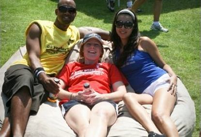 A man and two women all sitting on a 6', tan Fombag outdoors during the VAVI Kickball tournament