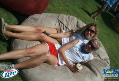 A couple of woman lounging in the center of a 6', tan Fombag during the VAVI kickball tournament