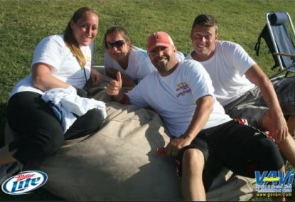 A group of four people, two men and two women, all relaxing on the 6', tan Fombag during the VAVI kickball tournament