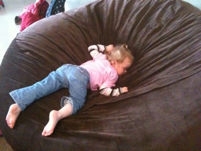 A picture of a small child sleeping, face down, in a giant, brown Fombag